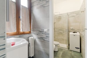 A bathroom with a white sink, a toilet, a shower with a glass door, and a radiator.
