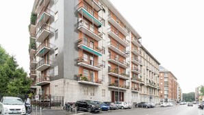 Un immeuble résidentiel à plusieurs étages, doté de balcons, avec des voitures garées et donnant sur la rue.