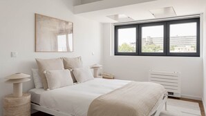 A bedroom with a bed, a window, a radiator, and a painting on the wall.