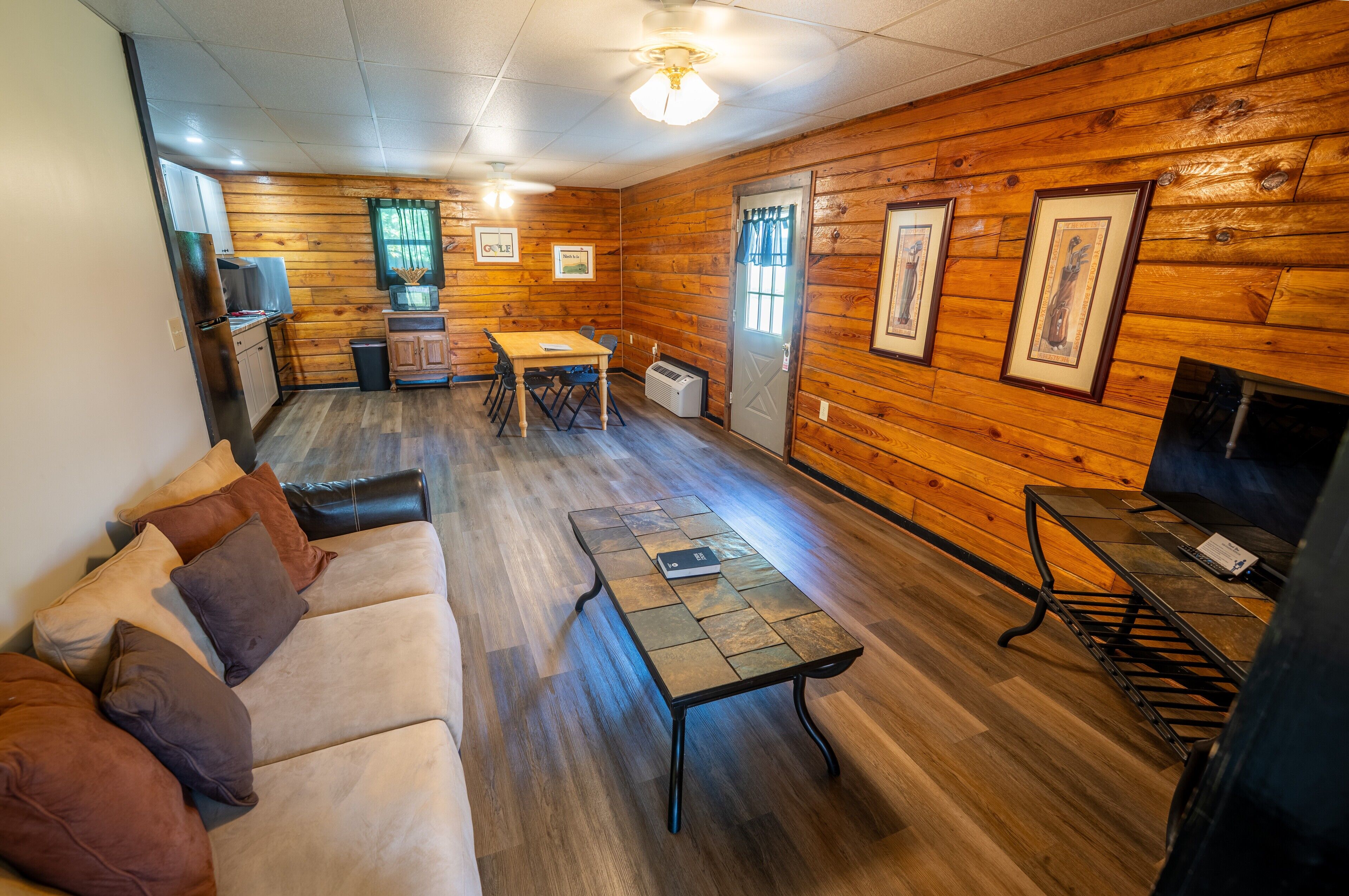 A cozy cabin interior with a wooden interior, a sofa, a dining table, and a TV.