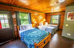 A cabin-style room with a large bed, two smaller beds, wooden walls, and a door with a window. - Fishtale Lodge (Buchanan)