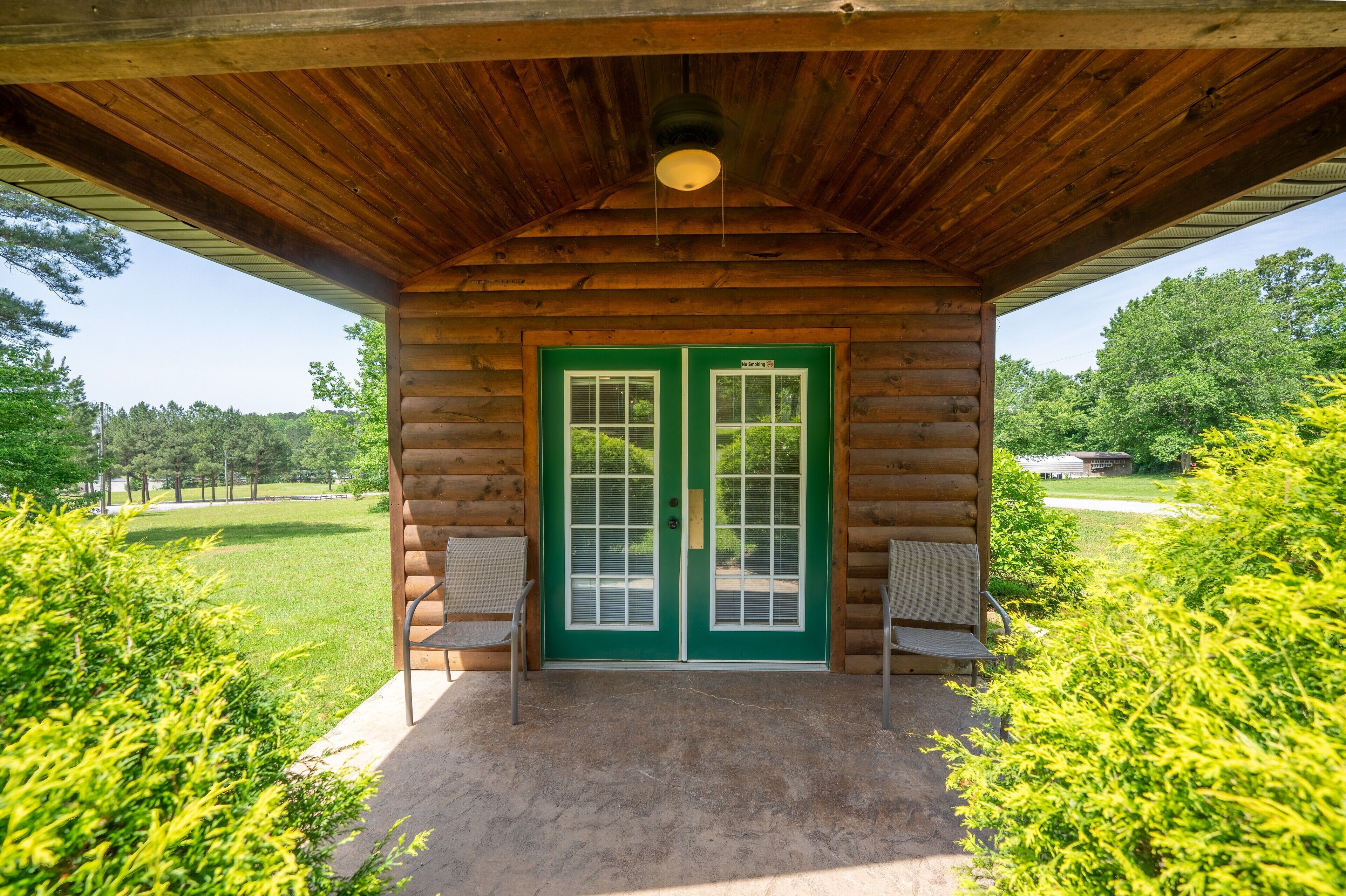 A log cabin with a green door, a covered porch, and two chairs.