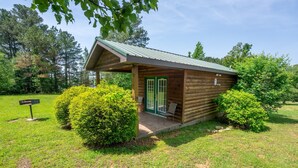 A small wooden cabin with a green door and a porch, surrounded by lush greenery and trees. - Fishtale Lodge (Buchanan)