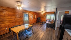 A cozy cabin interior with a wooden dining table, chairs, a television, and a refrigerator. - Fishtale Lodge (Buchanan)