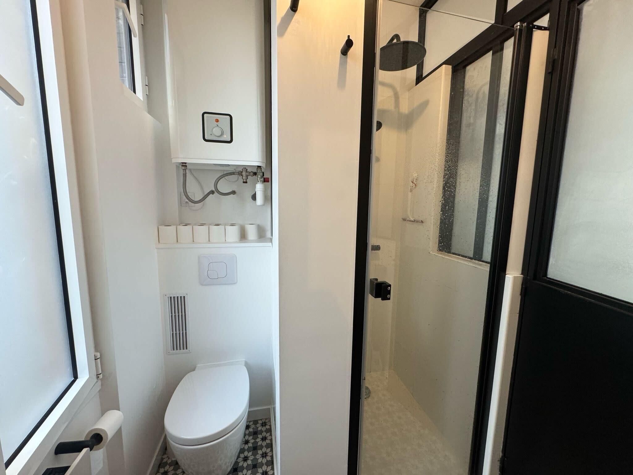 Une petite salle de bain comprenant des toilettes, un espace douche et un porte-rouleau de papier toilette.
