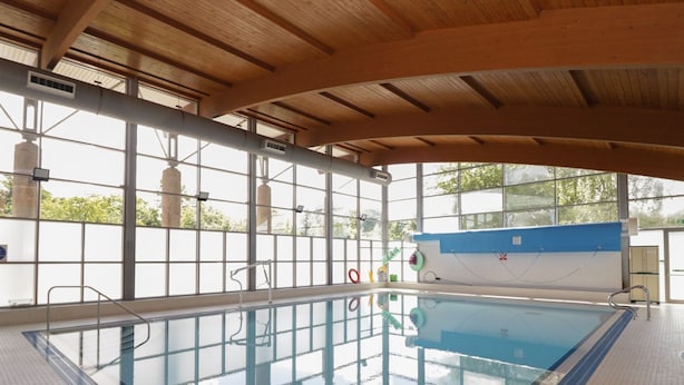 Ein Hallenbad mit klaren Glaswänden, Holzbalkendecke und gefliestem Boden.