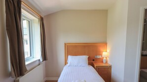Ein Hotelzimmer mit einem Einzelbett, einem Nachttisch mit Lampe und einem Fenster mit Vorhängen.
