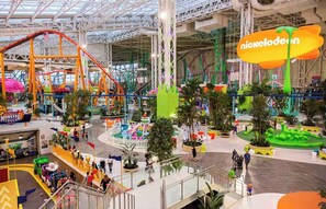 Un parque de atracciones interior vibrante con diversas atracciones y juegos, incluyendo un letrero de Nickelodeon.