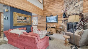 Ein gemütliches Wohnzimmer mit einem roten Sofa, einem grauen Sofa und einem Kamin aus Naturstein. Ein Fernseher ist an der Wand montiert und die Decke ist aus Holz.