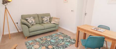 A small, cozy living area with a green sofa, a wooden dining table, and teal chairs.