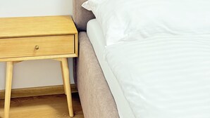 A bed with white bedding, a wooden nightstand, and a plain wall. - Riverside Apartment 12 (Hlavní město Praha)