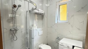A modern bathroom with a glass-enclosed shower, a toilet, a washing machine, and a small window. - Riverside Apartment 12 (Hlavní město Praha)