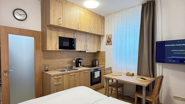 A compact hotel room with a bed, kitchenette, and a TV. - Riverside Apartment 12 (Hlavní město Praha)