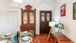 A dining area with a table set for a meal, a wooden cabinet, a door, and a lamp. - GuestHost - Charming 100 sqm apartment, accommodating up to 6 people, located on the ground floor of a typical Ligurian building.The property is located in the center of Cervo, one of Italy's most charming villages, in a convenient and well-served locati (Cervo)