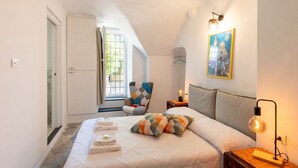 A bedroom with a bed, pillows, a chair, a nightstand, a lamp, a painting, and a door. - GuestHost - Charming 100 sqm apartment, accommodating up to 6 people, located on the ground floor of a typical Ligurian building.The property is located in the center of Cervo, one of Italy's most charming villages, in a convenient and well-served locati (Cervo)