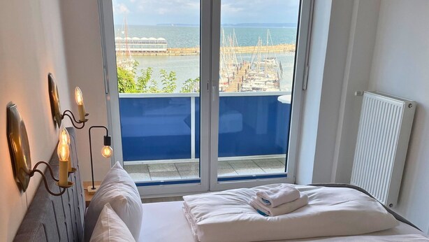 A hotel room with a bed, a nightstand, and a view of a marina through large windows. - FeWo im Hang direkt am Hafen, 6 Betten, 175m2 (Sassnitz)