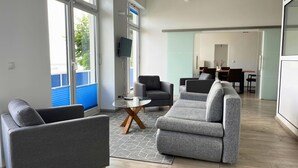 A modern living room with grey sofas, a coffee table, and a TV. There is a dining area with a table and chairs in the background. - FeWo im Hang direkt am Hafen, 6 Betten, 175m2 (Sassnitz)