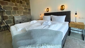 A neatly made bed with white linens and a grey throw blanket, two wall-mounted lamps, a wooden nightstand, and a stone wall. - FeWo im Hang direkt am Hafen, 6 Betten, 175m2 (Sassnitz)