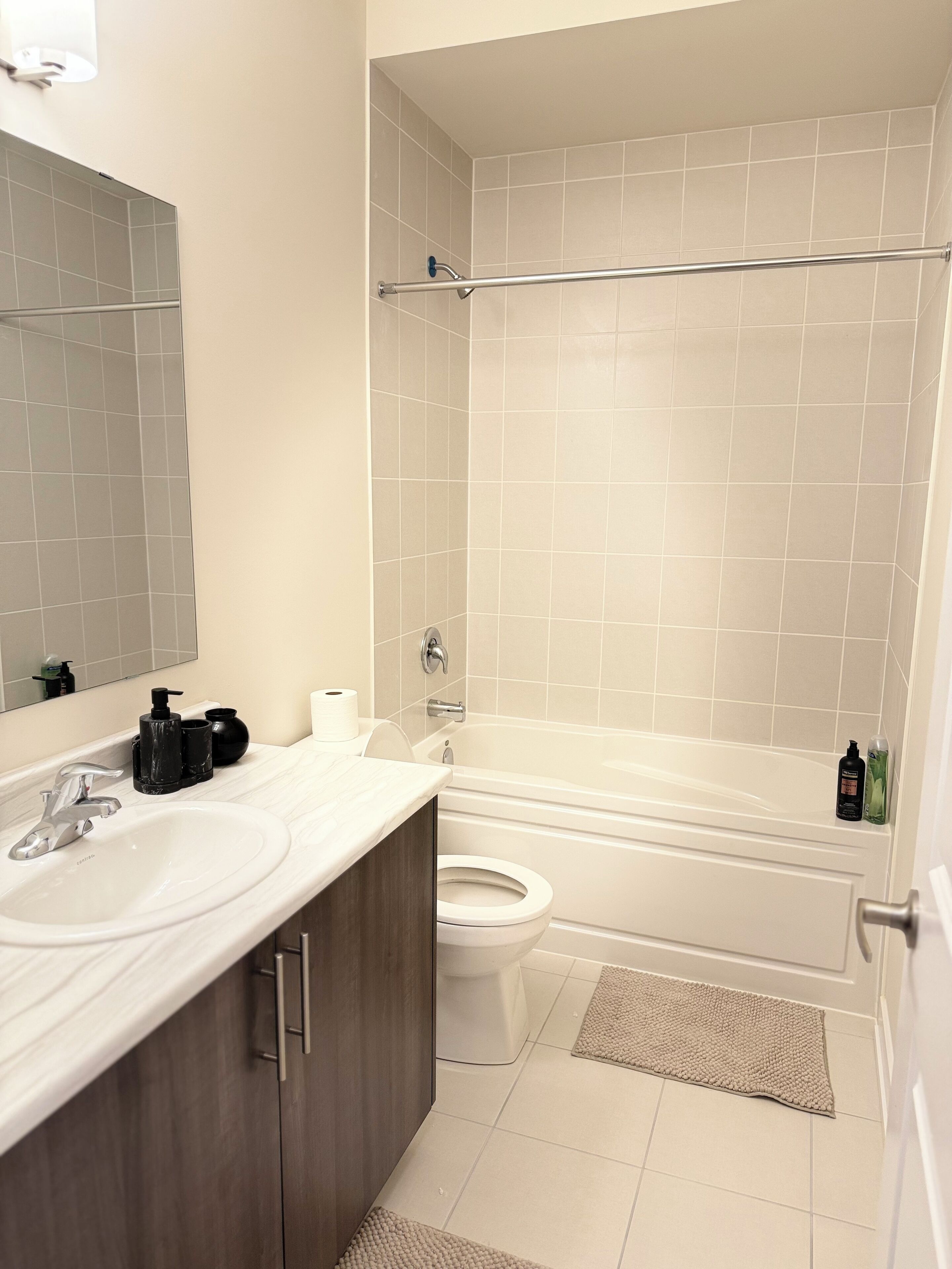 Ein modernes Badezimmer mit einem weißen Waschbecken, einem Spiegel und einer Toilette. Es gibt eine Badewanne mit einer Duschvorhang und einem Handtuchhalter.