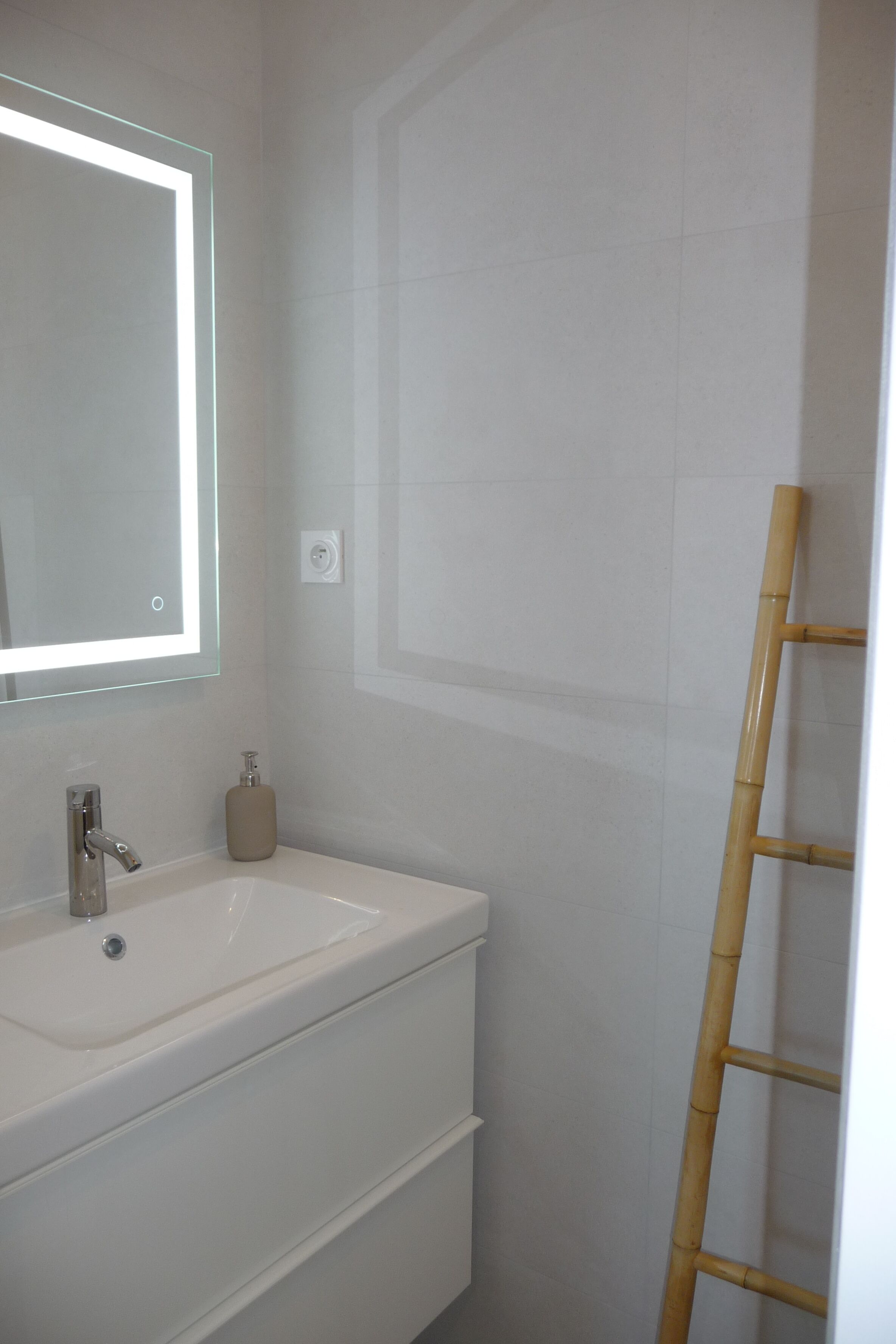 Un baño con un lavamanos blanco, un espejo y una escalera de bambú.
