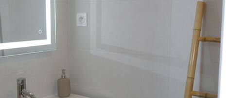 Un baño con un lavamanos blanco, un espejo y una escalera de bambú.