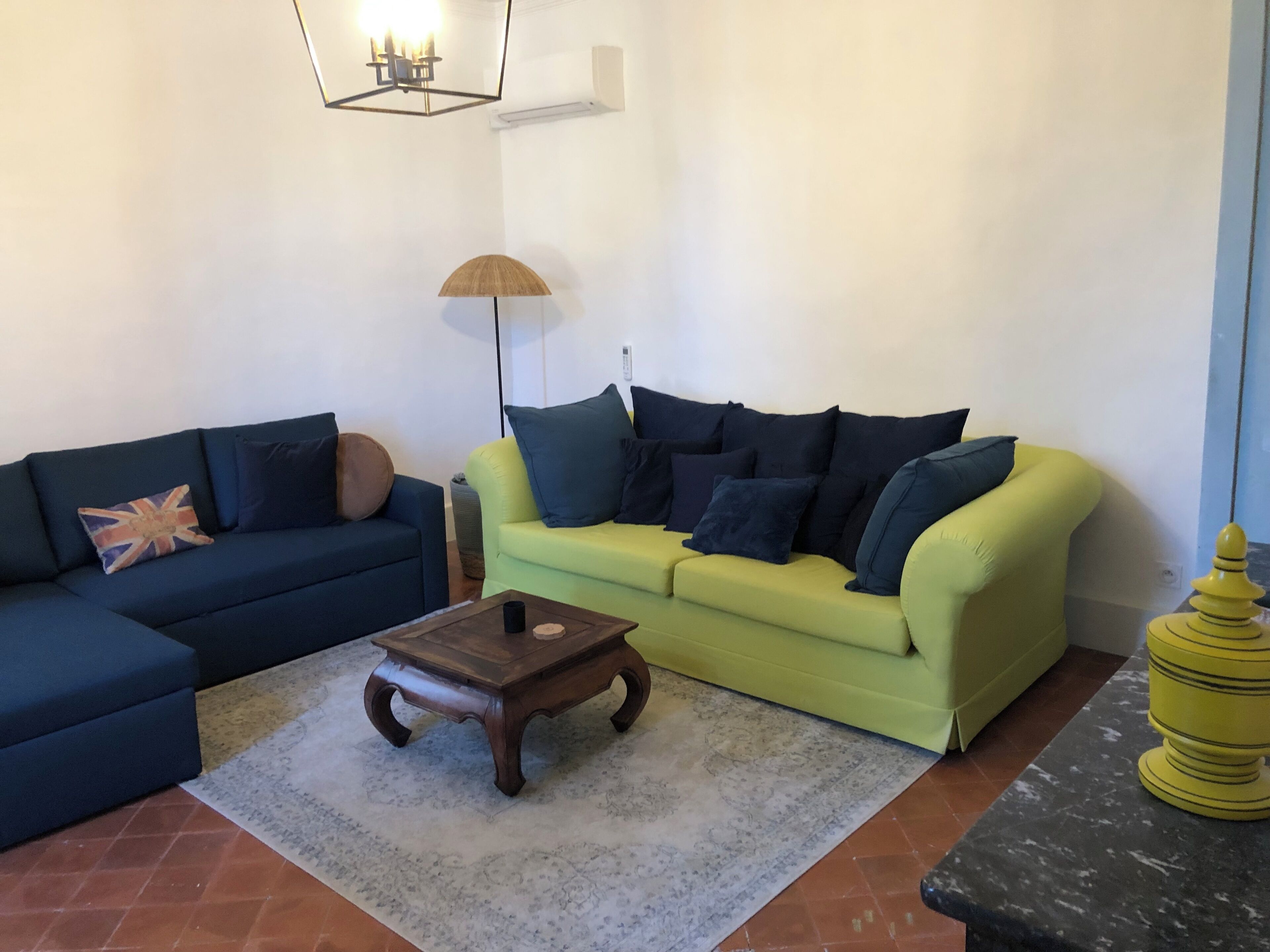 A living room with a blue sofa, a green sofa, a wooden coffee table, a floor lamp, and a yellow decorative item.