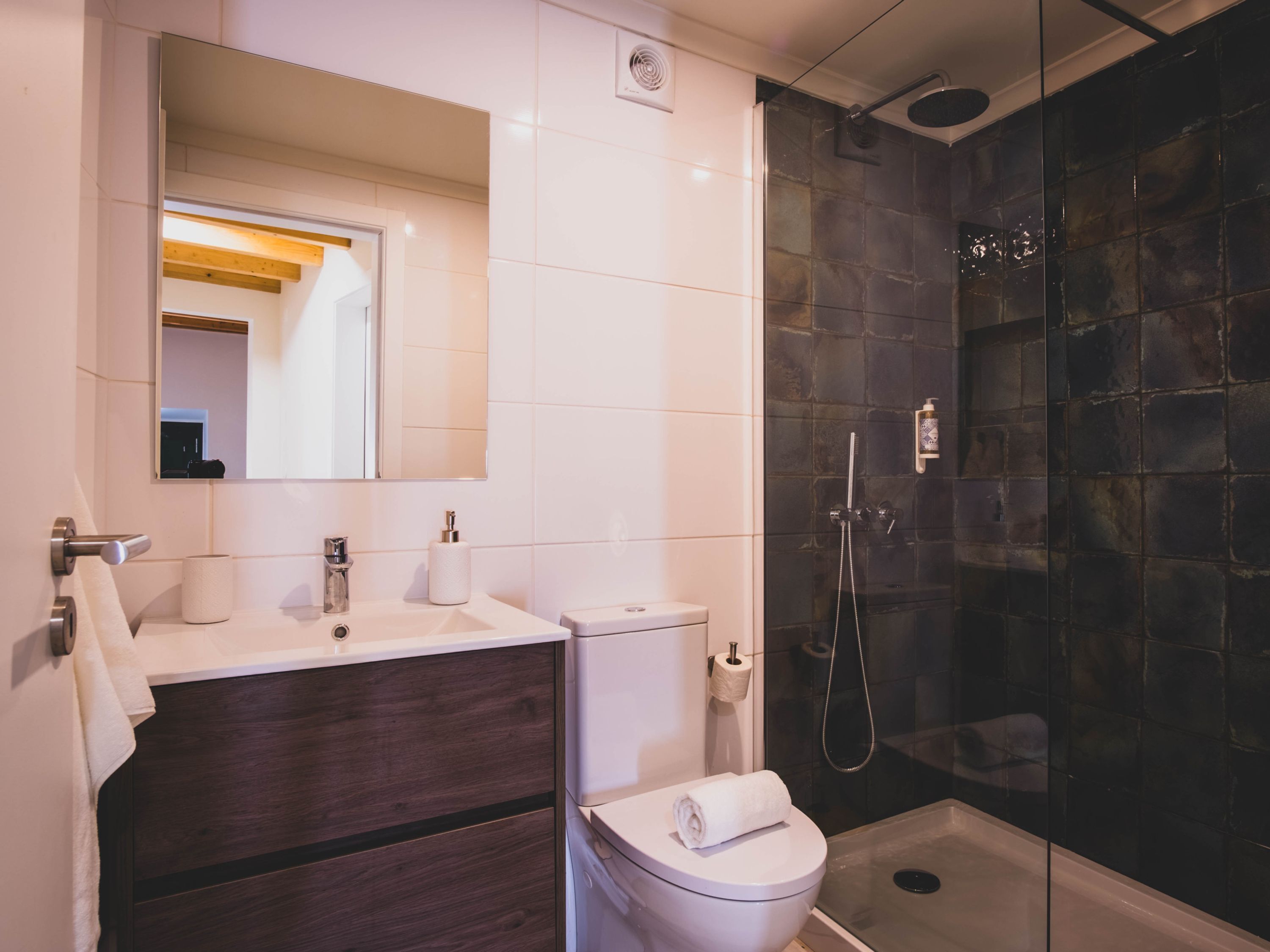 A modern bathroom with a white sink, dark wood vanity, a toilet, and a glass-enclosed shower.