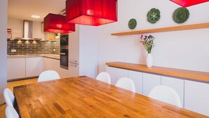 Een moderne keuken met witte kasten, een houten aanrecht en rode hanglampen. Er is een eethoek met een houten tafel en witte stoelen.