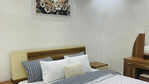 A neatly made bed with striped bedding, a wooden headboard, and a nightstand with a lamp. - Furnished studio in Mermoz (Dakar)