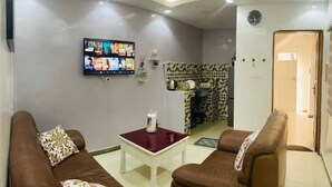 A living room with a flat-screen TV mounted on the wall, a small white table, and two brown sofas. - Furnished studio in Mermoz (Dakar)