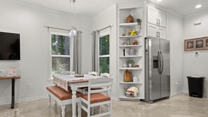 Une cuisine moderne avec des meubles blancs, un réfrigérateur en acier inoxydable et une table à manger avec des bancs.