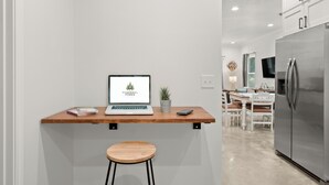 Une cuisine moderne avec un ordinateur portable posé sur un plan de travail en bois, une petite plante en pot et un réfrigérateur en acier inoxydable.