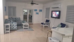 A living room with a sofa, two chairs, a TV, and a ceiling fan. - Charming cottage in Exuma for a relaxing getaway. Come and enjoy Hideaway Cove (Exuma)