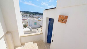 A narrow stairway leading to a blue door, with a view of a white building complex and a distant hill. - Relax in Leuca - Terrace with Panoramic Sea View - Casa Michele (Santa Maria di Leuca)