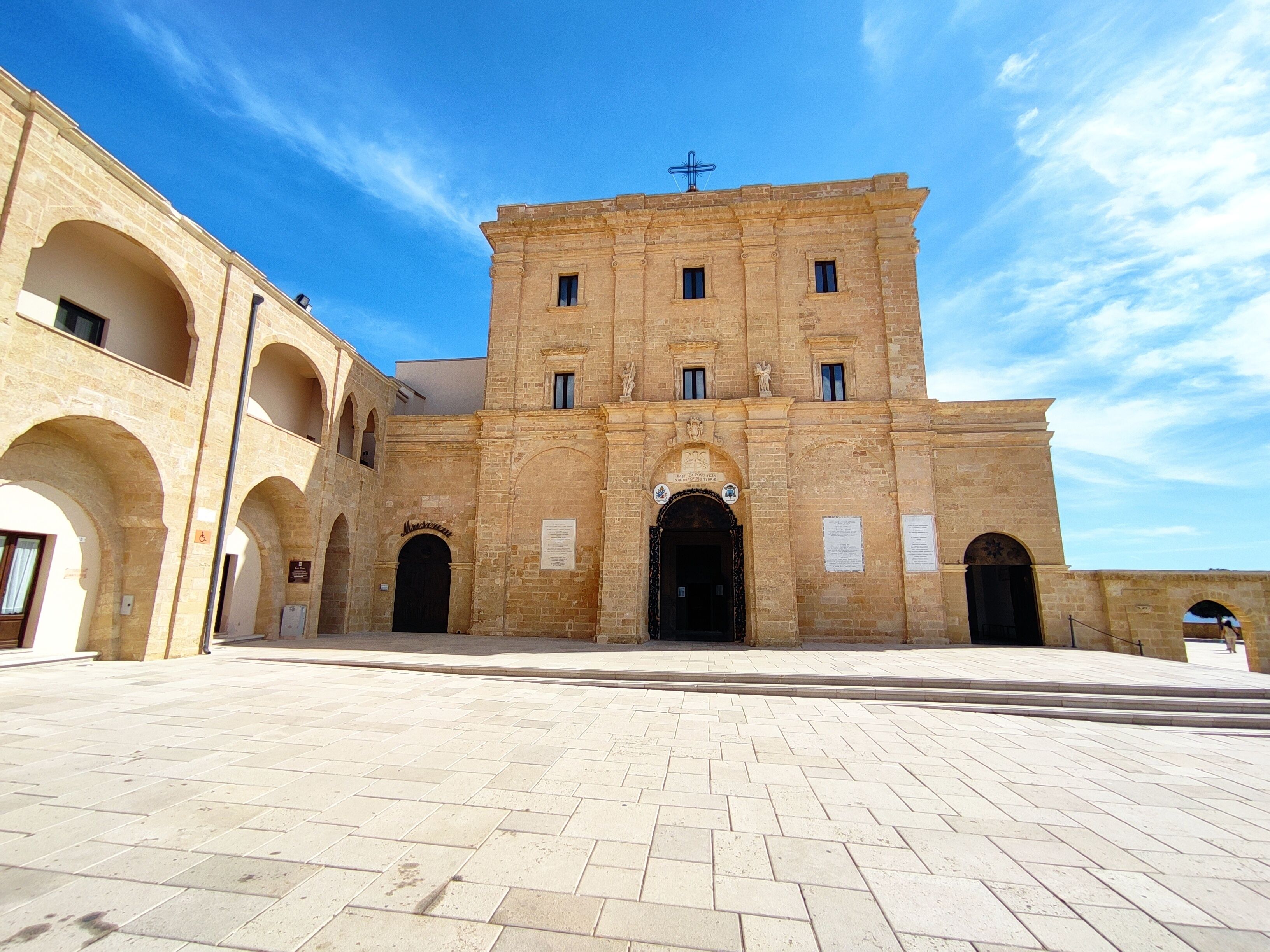 Un edificio histórico con una entrada central, arcos y una cruz en la parte superior.