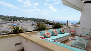 A rooftop terrace with a sofa, chairs, and a glass table, overlooking a coastal town. - Relax in Leuca - Terrace with Panoramic Sea View - Casa Michele (Santa Maria di Leuca)