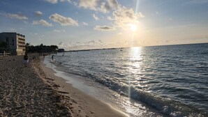 A beach with a clear sky, calm sea, and buildings in the background.