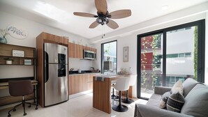 A modern kitchen with a built-in refrigerator, microwave, and wooden cabinets. There is a dining area with a bar stool and a sofa with cushions.