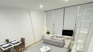 A modern bedroom with a bed, a small table with chairs, a TV, and a wardrobe. - Melhores Flats - Deslumbrante  (Joao Pessoa)