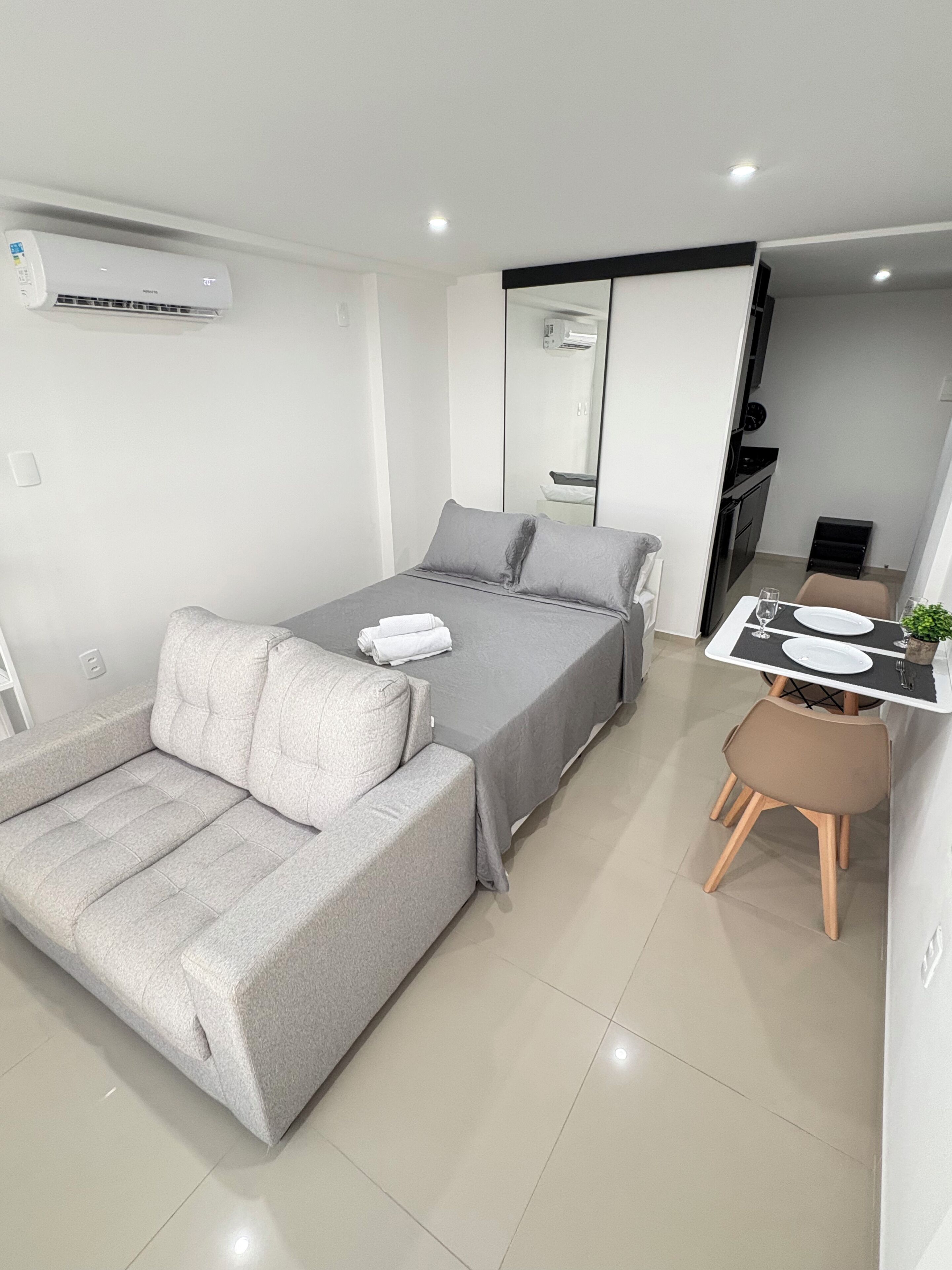 Una camera da letto moderna con un letto, un divano, un tavolo da pranzo con sedie e un condizionatore d'aria.
