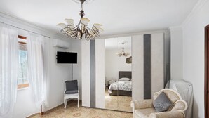 Een slaapkamer met een bed, een stoel, een bank, een televisie, een spiegel en een kroonluchter.