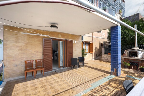 A residential building with a tiled patio, wooden chairs, a small table, and a brick wall.