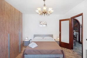 Ein Schlafzimmer mit einem Bett, Nachttischen, einer Chandelierleuchtre, einem Kleiderschrank und einer Tür zu einem anderen Raum.