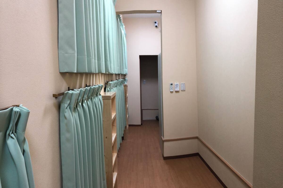 Um corredor com piso de madeira, paredes claras e uma fileira de cortinas azul claro à esquerda.