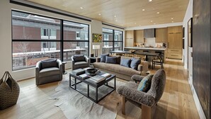 A spacious living area with a sofa, armchairs, and a coffee table. Large windows provide a view of the outside.
