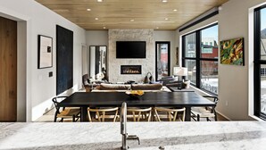 A modern dining area with a marble countertop, a large dining table, and chairs. There is a stone accent wall with a flat-screen TV mounted above it.