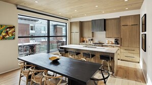 A modern kitchen with wooden cabinets, a large island with bar stools, and a view through large windows.