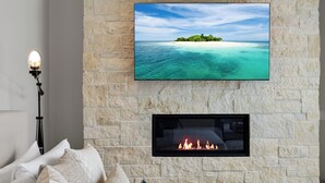 A bedroom with a stone wall, a flat-screen TV, a fireplace, and a bed with pillows.