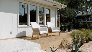 Una casa moderna con un porche cubierto, dos sillas blancas y una terraza de madera.