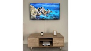 Un televisor de pantalla plana montado en la pared, sobre un mueble de televisión de madera con un reloj y libros.